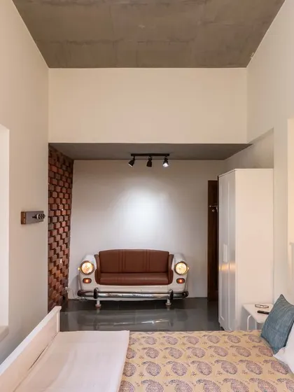 A unique sofa made from the front of an old car sits in the bedroom, an example of playful upcycling. This piece serves as a focal point and a conversation starter, reflecting the client's personality within the design.