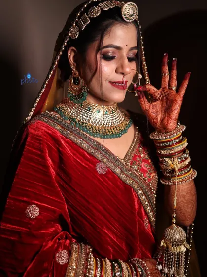 A classic bridal pose showing off the intricate mehndi design on the bride's hand as she adjusts her nose ring.