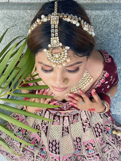 A detailed shot focusing on the bridal matha patti and eye makeup. The soft, warm tones on the eyes complement the elaborate pearl and kundan headpiece perfectly.