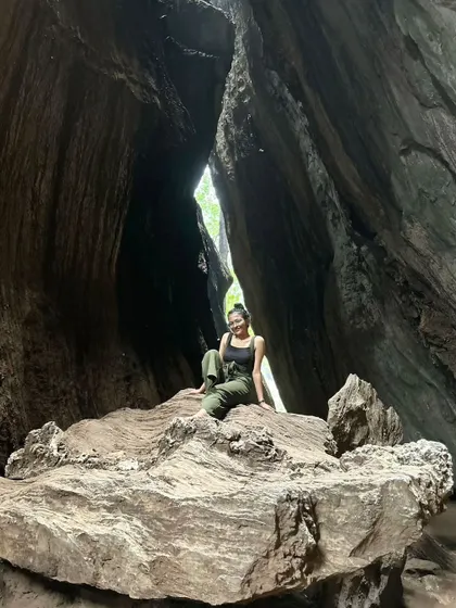 Sitting on a large rock inside a cave. This photo from my travels highlights my adventurous side and my comfort in natural, rugged environments.