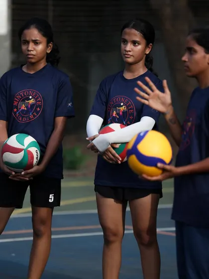 Young players listen to instructions, holding their volleyballs and ready for the next drill. An eagerness to learn is the first step to greatness.