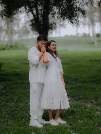 A tender moment where the groom kisses his fiancée's hand, set against the soft, natural light of a forest.