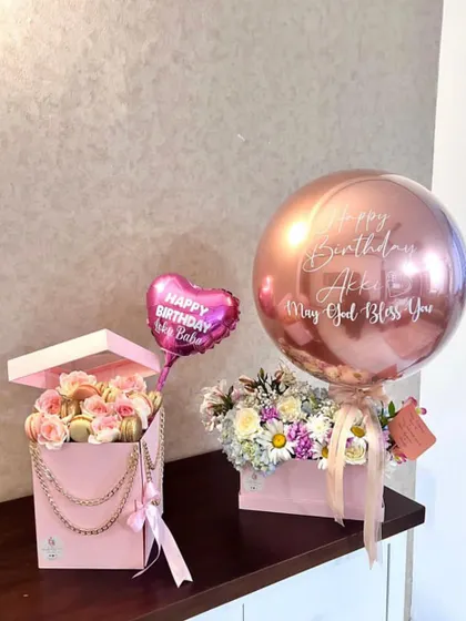 A coordinated birthday gift set in shades of pink. It features a flower box with a personalized rose gold balloon, alongside a separate box of macarons and roses with a mini heart balloon.