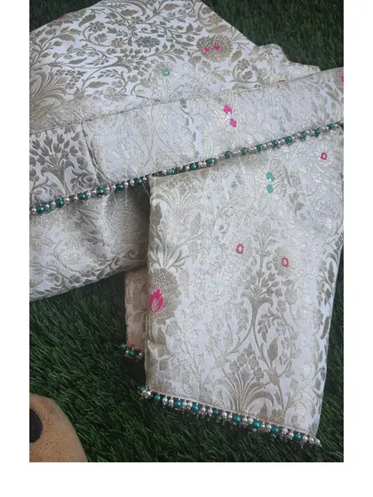 A detail shot of the off-white brocade fabric used for the blouse, featuring delicate pearl and bead work along the sleeve hem.