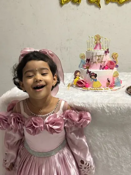 The birthday princess with her big, happy smile, standing proudly next to her two-tier princess cake. These are the memories that last a lifetime.