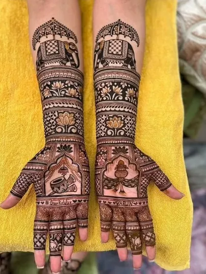 A stunning example of symmetrical bridal mehndi. Both hands feature bands of decorated elephants, lotus flowers, and personalized elements like names and auspicious symbols for the wedding.