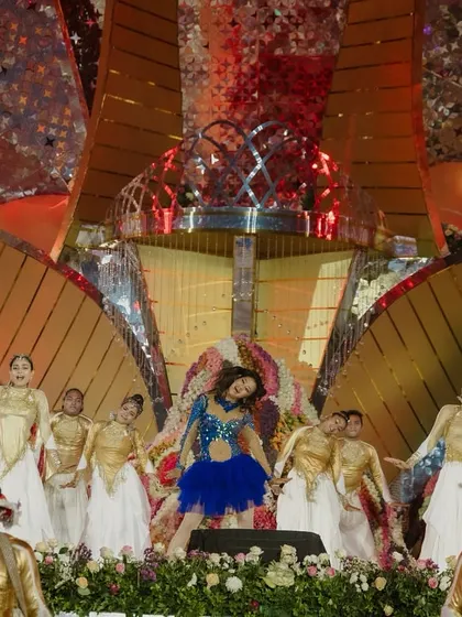 The lead dancer takes center stage in a vibrant blue outfit, surrounded by a troupe in gold, creating a dynamic and colorful performance.