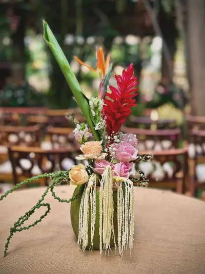 The table centerpieces featured a mix of tropical flowers like red ginger lily and roses, arranged in simple green vases. These arrangements added a pop of colour to the rustic tablescapes while maintaining a natural, garden feel.