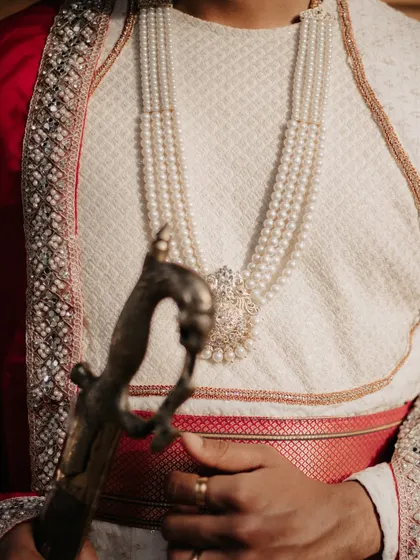 A detail shot focusing on the groom's pearl necklace and the hilt of the ceremonial sword he is holding.