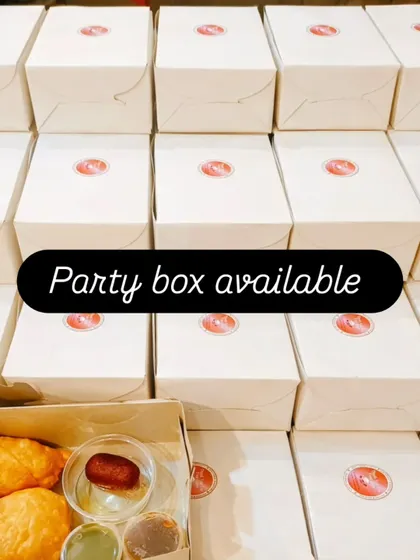 Samosa, a sweet and chutneys sit in an open snack box beside the closed party boxes we have packed.