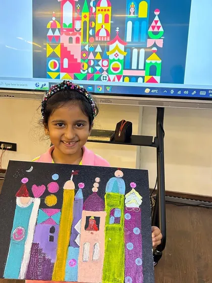 A proud student from our summer art camp displays her colorful castle painting, inspired by the artist Mary Blair. Our classes often explore art history in a fun and accessible way.