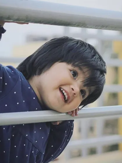 A baby's smile can brighten any day. This candid shot captures a moment of pure, simple happiness as she peeks through the railings during an outdoor shoot.