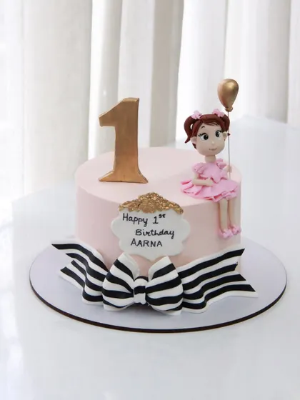 A chic and sweet 1st birthday cake for Aarna, featuring a stylish black and white striped bow and a cute girl topper.