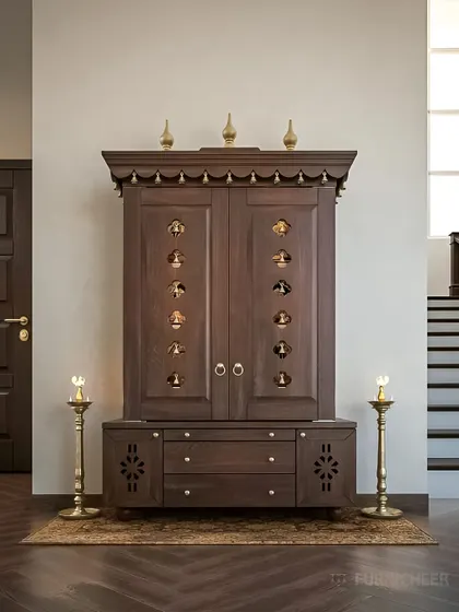 This is a classic, freestanding pooja cabinet crafted from dark wood. It features doors with small, bell-shaped cutouts, multiple drawers, and a traditional top cornice, resembling a temple structure.