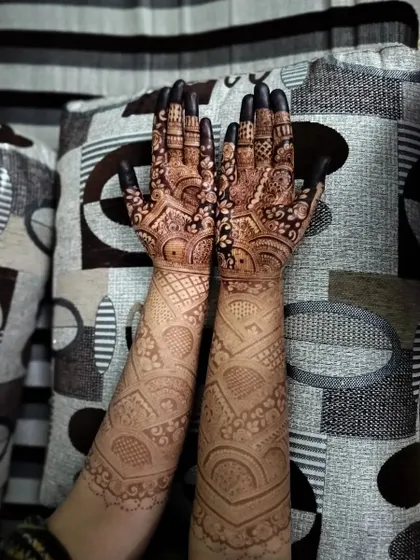 The beautiful result of a bridal henna session, showing the dark, rich paste before it's removed. The design features geometric and architectural elements.