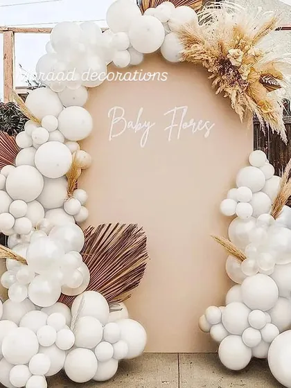 This boho-chic backdrop is perfect for a baby shower, with "Baby Flores" written on a neutral-toned panel. The all-white balloon garland is complemented by dried pampas grass and palm leaves for a natural and trendy look.