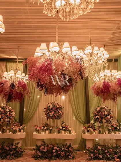 A wider view of the floral chandelier installation. The layers of color and texture, from deep burgundy to soft pinks, created a stunning visual against the soft green and cream drapes.