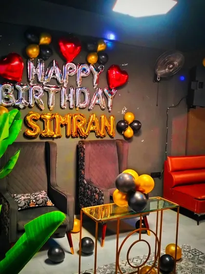 A close-up of the birthday setup for Simran, showing the gold, black, and silver balloons with heart-shaped foil accents.