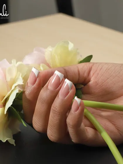 A beautiful shot of a fresh French manicure, with the client holding flowers. It's a perfect look for any occasion.