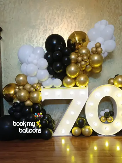 Celebrating 70 years in style. This elegant black, white, and gold balloon arrangement surrounding large marquee numbers creates a timeless and classic look for a major milestone birthday.