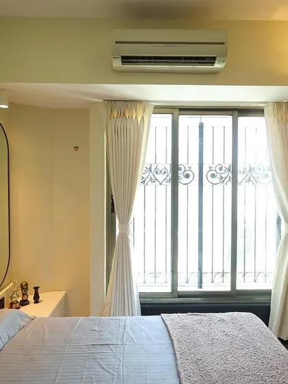 The serene bedroom retreat features a soft pink headboard, an arched wall panel, and an elegant oval mirror, creating a harmonious and stylish space.