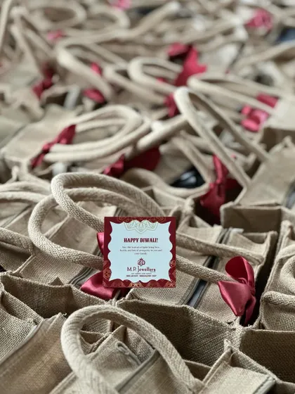 A close-up of the custom-branded jute bags for M.P. Jewellers, complete with a "Happy Diwali" tag and a bright red ribbon.