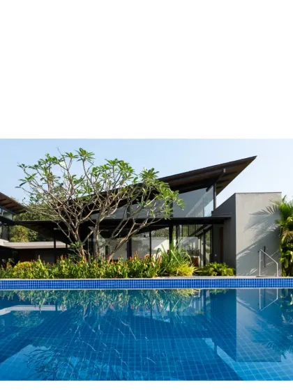 A pool reflects the sky and the simple, sloped roof of an Alibaug home. These country dwellings are designed for city dwellers seeking a different pace of life, with high roofs for cooling and local stone for durability.