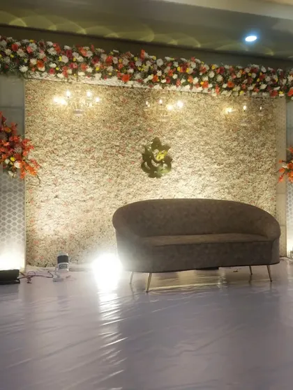 A closer view of the stage, focusing on the texture of the dense white floral backdrop and the simple, curved sofa for the couple.