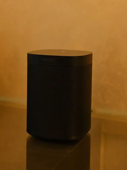 A modern Sonos speaker placed on a glass shelf. Its clean, minimal design allows it to fit into any contemporary home, providing high-quality wireless audio without disrupting the room's elegant and warm aesthetic.