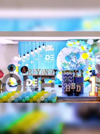 A fun and colorful baby elephant theme for Riyansh's first birthday. This setup includes large 'ONE' marquee letters, character cutouts, and a backdrop with twinkling lights.