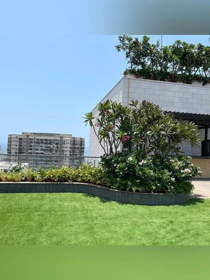 This rooftop features a pristine artificial lawn bordered by a curved planter filled with flowering shrubs. The design maximizes green space while providing a durable, low-maintenance surface for use year-round.