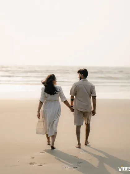 A couple walks hand-in-hand away from the camera along the shoreline. This classic pre-wedding beach photo symbolizes their journey forward together.