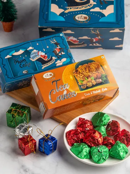 The Festive Joy Hamper combines our Rich Plum Cake, Date & Walnut Tea Cake, and a bowl of assorted chocolate rocks. It's a delightful mix of cake and confections for the holidays.