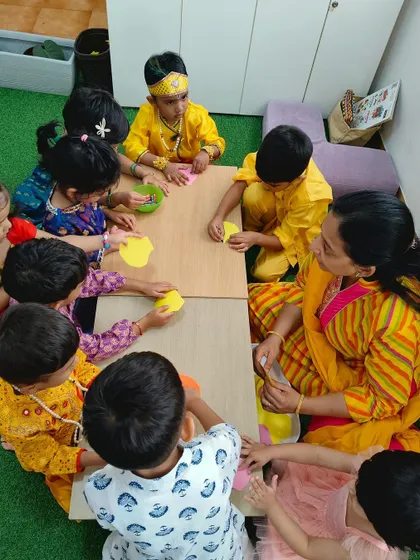 A teacher and children dressed in yellow for Janmashtami work on a craft together. We create an immersive environment for every festival.