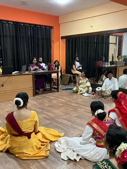 Students seated on the floor, awaiting their turn for the practical exam in front of the panel of examiners and musicians.