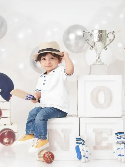 The little champion poses with his trophy in a full cricket-themed setup, complete with 'ONE' blocks for his first birthday.