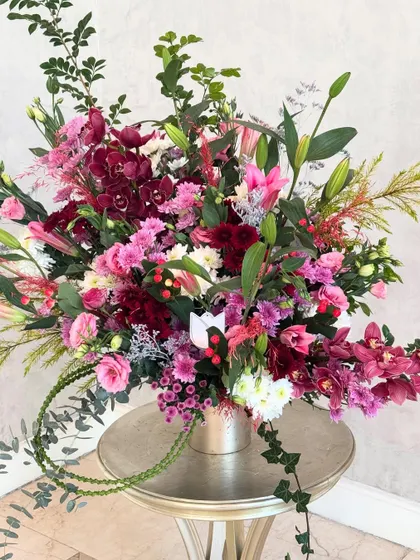 A lush and celebratory "Congratulations" arrangement. The design is a wild and beautiful mix of pinks and burgundies, with orchids, lilies, and roses creating a feeling of joyful abundance.