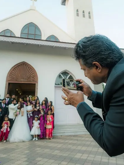 A behind-the-scenes moment at a Christian wedding. A guest captures a group photo in front of the church, showing the importance of family and friends in the celebration.