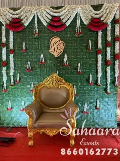 A close-up of our traditional baby shower backdrop. The design features a woven green mat, garlands of jasmine and roses, and a wooden cutout symbolizing motherhood.