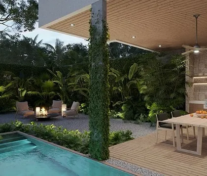 This patio design at night showcases a beautiful blend of features. We included a narrow lap pool, an outdoor kitchen and dining area, and a cozy fire pit lounge, all surrounded by dense, tropical-style greenery.