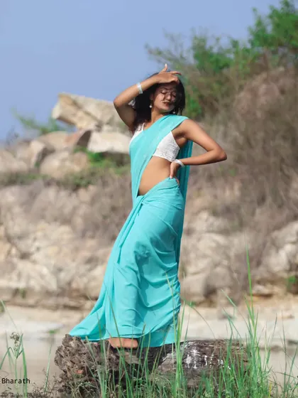 A dynamic portrait that captures the beauty of the flowing saree against a natural, rocky backdrop near the water.