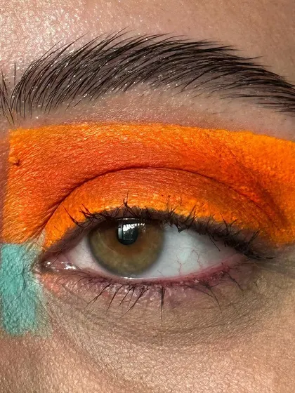 A slightly different angle of the graphic orange and teal eye look. The clean lines and intense pigment are key to achieving this striking editorial style.