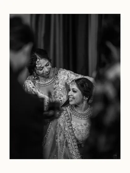 A candid black and white moment between the bride and her sister or friend, sharing a laugh while getting ready. It captures the joy and support system on the wedding day.