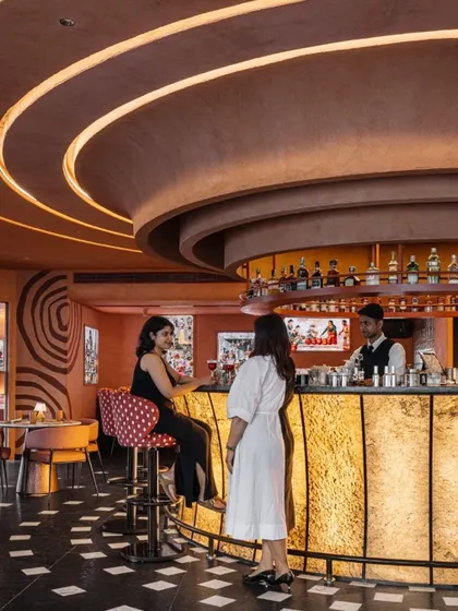 The bar at Idylll is a social hub, with a curved, glowing counter and layered ceiling details that draw the eye. The design encourages interaction and creates a high-energy atmosphere.