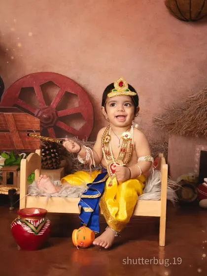 A joyful little Kanha sitting on his bed, surrounded by the sights of a rustic village.
