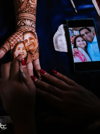 A behind-the-scenes look at the master mehendi artist meticulously painting a portrait of the bride's parents onto her hand.