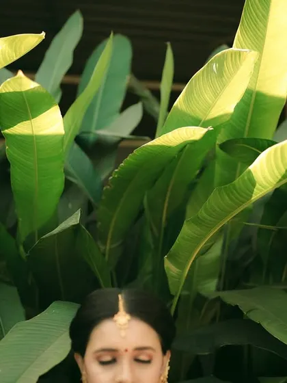 An artistic shot with the bride's face framed by large green leaves, creating a natural and beautiful composition.