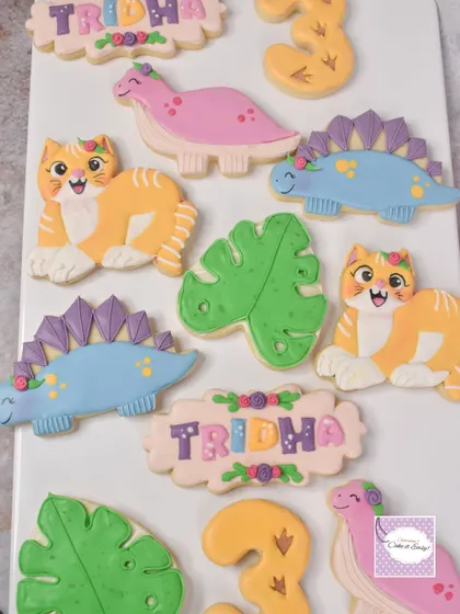 A fun twist on a popular theme: a dinosaur cake for a little girl turning three. We used a pastel color palette and added some cute cats to the matching cookie set by special request.
