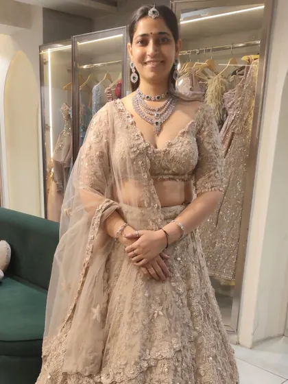 A happy client trying on a beautiful American Diamond necklace with a blue stone. It pairs perfectly with her elegant beige lehenga, creating a sophisticated look for an evening event.
