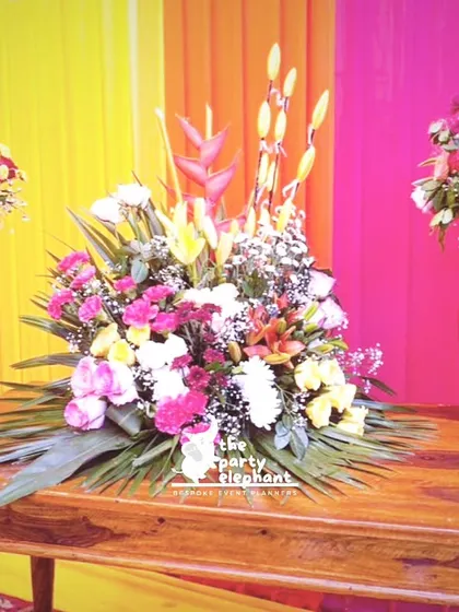 A beautiful floral arrangement in hammered metal vases, set against a backdrop of colorful drapes, adding a touch of elegance to the vibrant Mehendi decor.